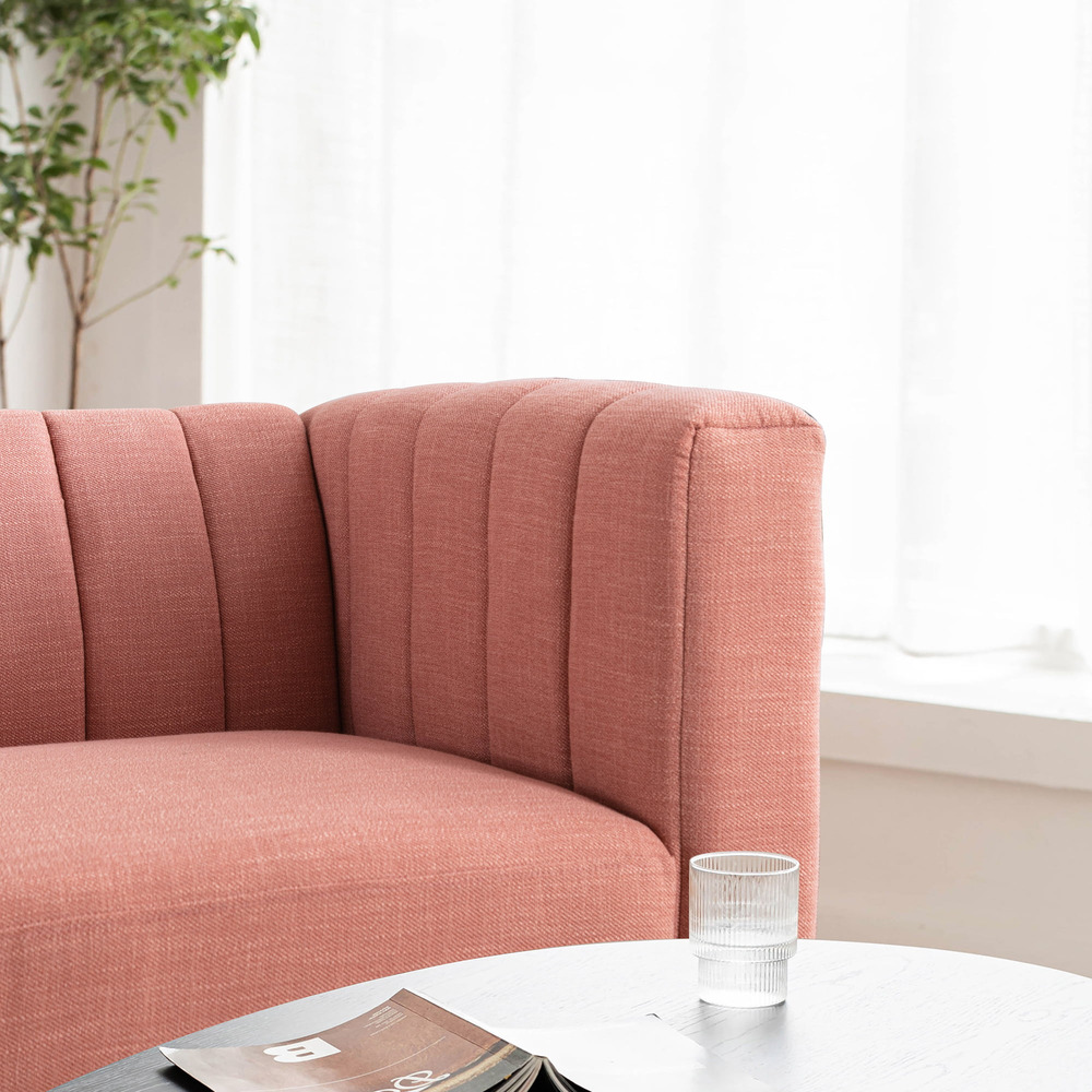 Ảnh cận cảnh góc tay vịn và tựa lưng của sofa màu hồng nhạt, thể hiện rõ các đường may dọc tạo rãnh tinh tế. Bên cạnh là m…