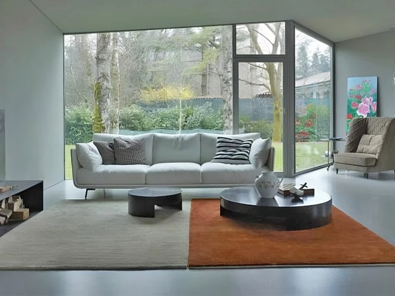 Sofa băng Joeerly SF-329 màu trắng ngà được đặt trong một phòng khách hiện đại với cửa kính lớn nhìn ra sân vườn. Góc chụp…