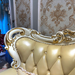 Chi tiết phần lưng tựa và tay vịn của sofa, với các đường cong mềm mại và họa tiết dát vàng nổi bật trên nền da màu kem. N…