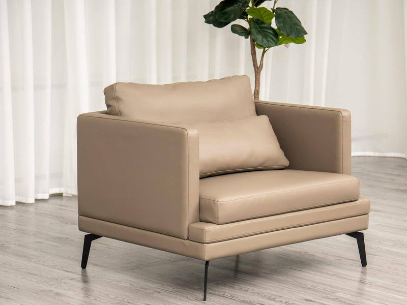Ghế sofa đơn BM001-113-C1050 màu nâu be với đệm tựa lưng và gối ôm nhỏ, đặt trong không gian phòng khách có rèm trắng và c…