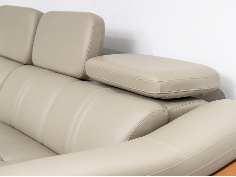 Cận cảnh phần tựa đầu điều chỉnh và góc nối của sofa da màu be/ghi sáng. Chụp từ góc trên xuống, làm rõ các đường may tinh…