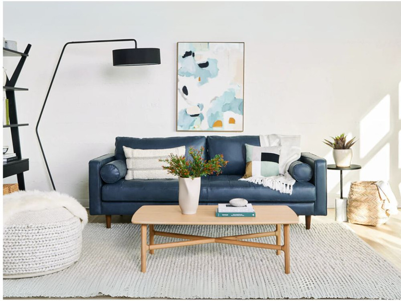 Phòng khách hiện đại với sofa băng màu xanh navy, bàn trà gỗ sáng màu, thảm trắng và đèn sàn cong. Bức tranh treo tường tr…