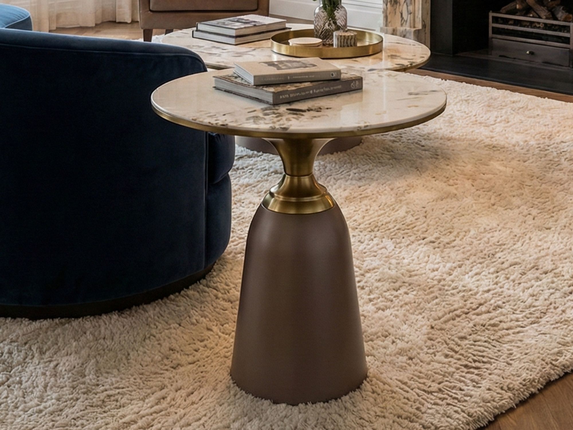 Bàn trà góc BG216 đặt cạnh ghế sofa xanh đậm trong không gian phòng khách ấm cúng với thảm lông màu kem. Bàn có mặt đá vân…