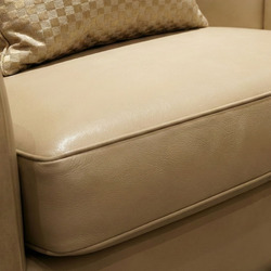 Cận cảnh phần đệm ngồi và tựa lưng của ghế sofa, với lớp bọc da sinh thái màu be nhạt căng mịn. Các đường may tinh xảo, ch…