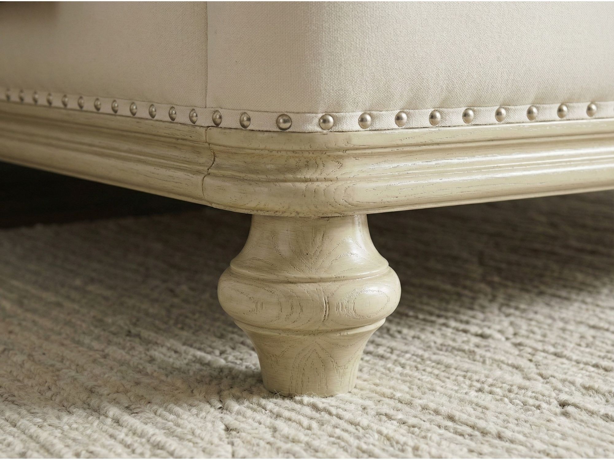 Chi tiết chân giường GI2803-18 hình trụ tròn tiện hoa văn, sơn màu vàng nhạt, đặt trên thảm lông màu trắng. Phần viền khun…