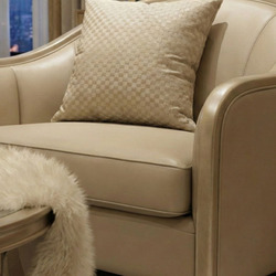 Cận cảnh tay vịn và gối tựa của ghế sofa đơn, với lớp bọc da sinh thái màu be nhạt. Gối tựa nhỏ họa tiết hình học màu vàng…