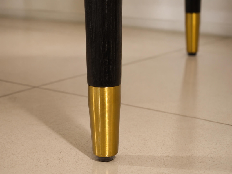 Cận cảnh chân ghế gỗ sồi đen của ghế ăn Bentley, với phần đế được bọc đồng vàng sáng bóng. Chi tiết này không chỉ tăng tín…