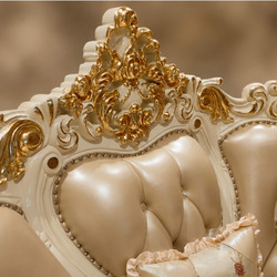 Chi tiết phần tựa lưng ghế sofa, với các đường cong mềm mại và nút rút bọc da màu kem. Phía trên là họa tiết chạm khắc dát…