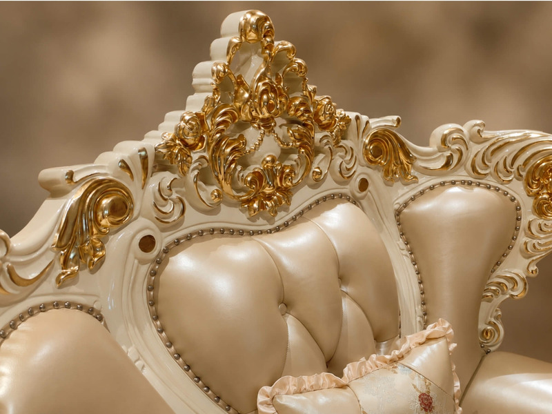 Chi tiết phần tựa lưng ghế sofa, với các đường cong mềm mại và nút rút bọc da màu kem. Phía trên là họa tiết chạm khắc dát…