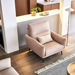 Sofa đơn ELLY màu hồng nhạt, bọc da cao cấp, đặt trong không gian phòng khách hiện đại với sàn gỗ và thảm. Ghế có chân kim…
