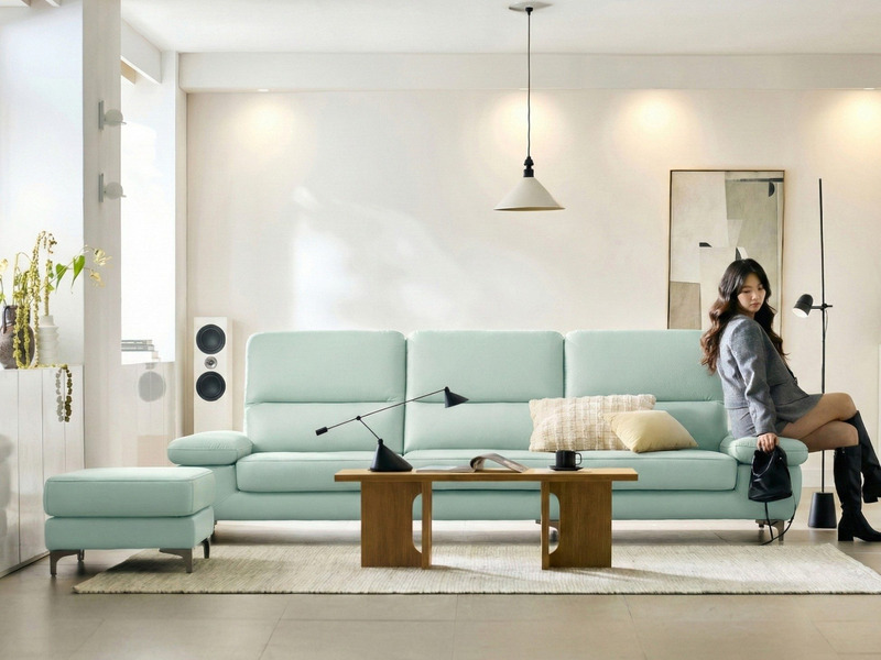 Sofa băng FEATHER màu xanh pastel, góc chụp từ phía trước hơi chếch, một người phụ nữ ngồi thư giãn trên sofa. Sofa có tay…