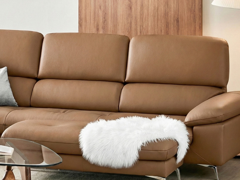 Góc cận cảnh sofa Ravell chữ L màu nâu latte, tập trung vào phần tay vịn kiểu daybed rộng rãi và mềm mại, có gối lông trắn…