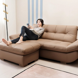 Hình ảnh tổng thể sofa SOFFLE màu nâu latte, kiểu dáng băng chữ L hiện đại, với một người phụ nữ đang ngồi thư giãn, tựa l…