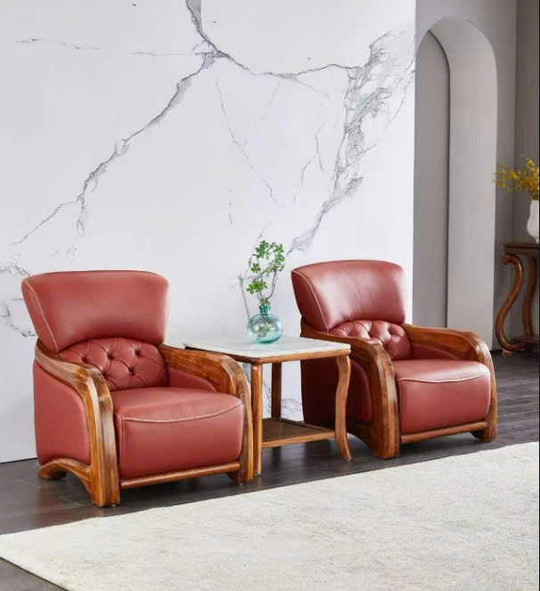 Hai ghế sofa đơn màu đỏ đô, khung gỗ mun tự nhiên, được đặt trong không gian phòng khách trang nhã với tường ốp đá marble…