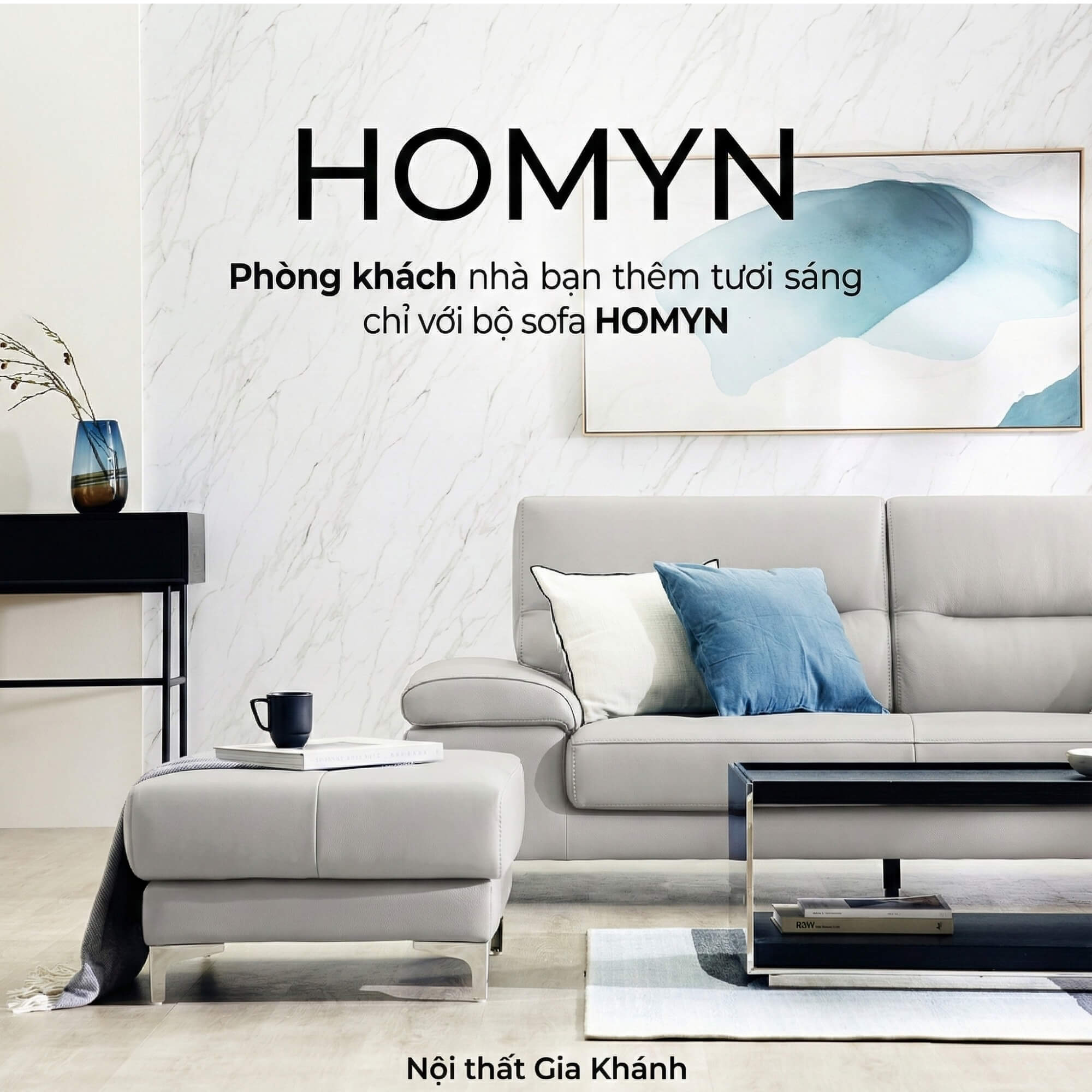 Sofa HOMYN màu xám nhạt trong phòng khách hiện đại, chụp chính diện. Sofa kết hợp ghế đôn, bàn trà mặt đá đen và thảm trải…