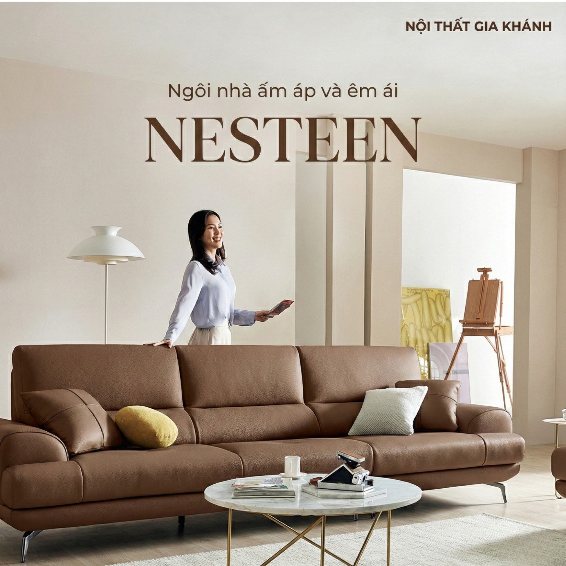 Sofa băng NESTEEN bọc da màu nâu, đặt trong phòng khách hiện đại với tường be và sàn gỗ. Người mẫu nữ đứng cạnh sofa, tổng…