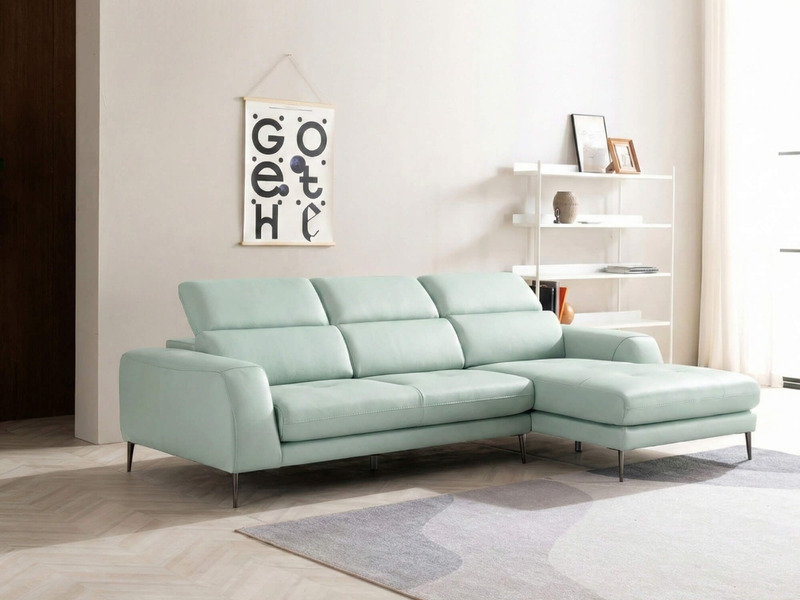 Sofa góc da màu xanh bạc hà nhạt, chụp toàn cảnh từ phía trước bên phải, đặt trong phòng khách hiện đại với tường trắng, k…