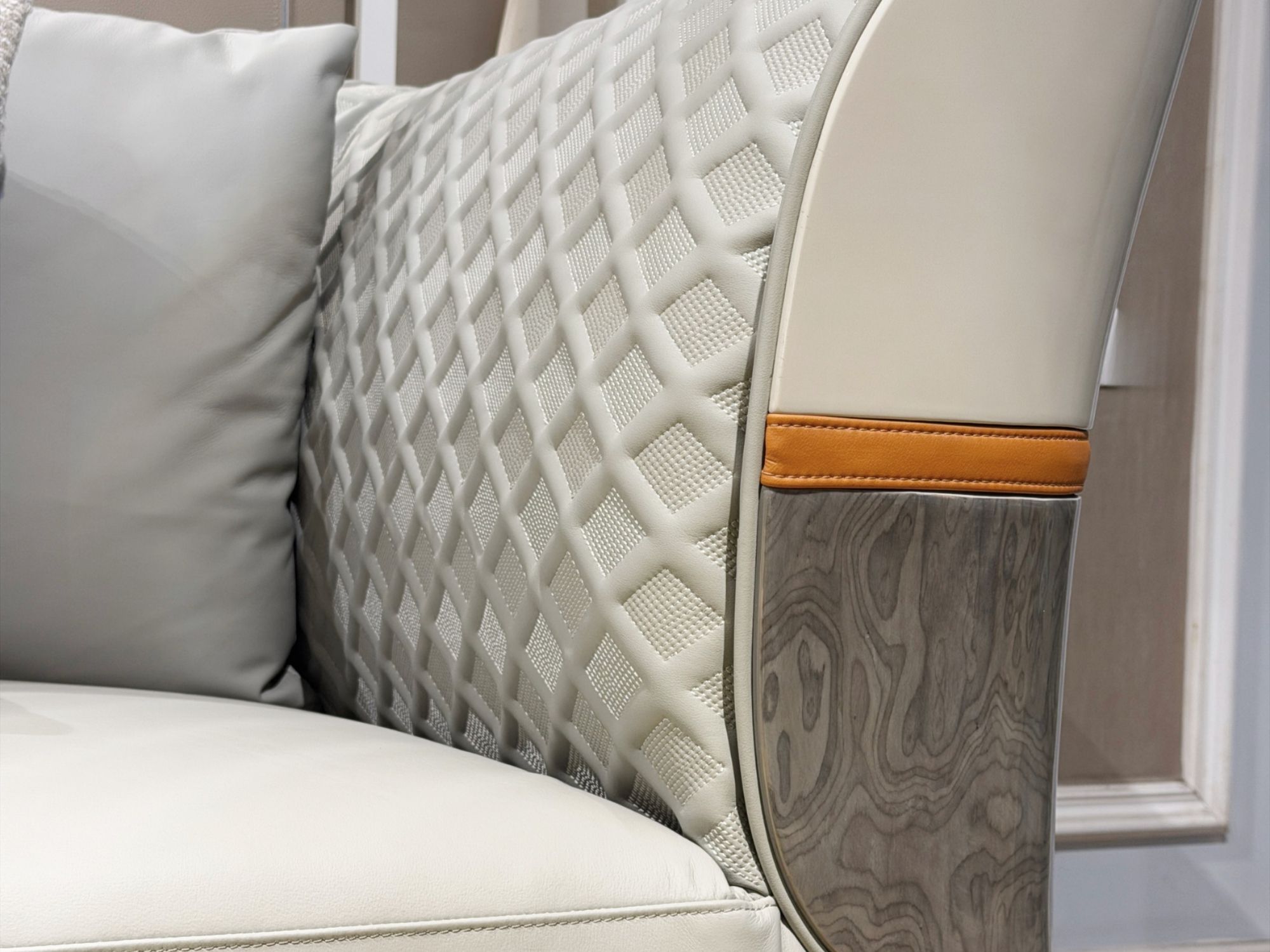 Góc cận của tay vịn sofa, nổi bật với phần da bò màu trắng kem được chần trám tinh tế, kết hợp dải da màu nâu cam và ốp gỗ…