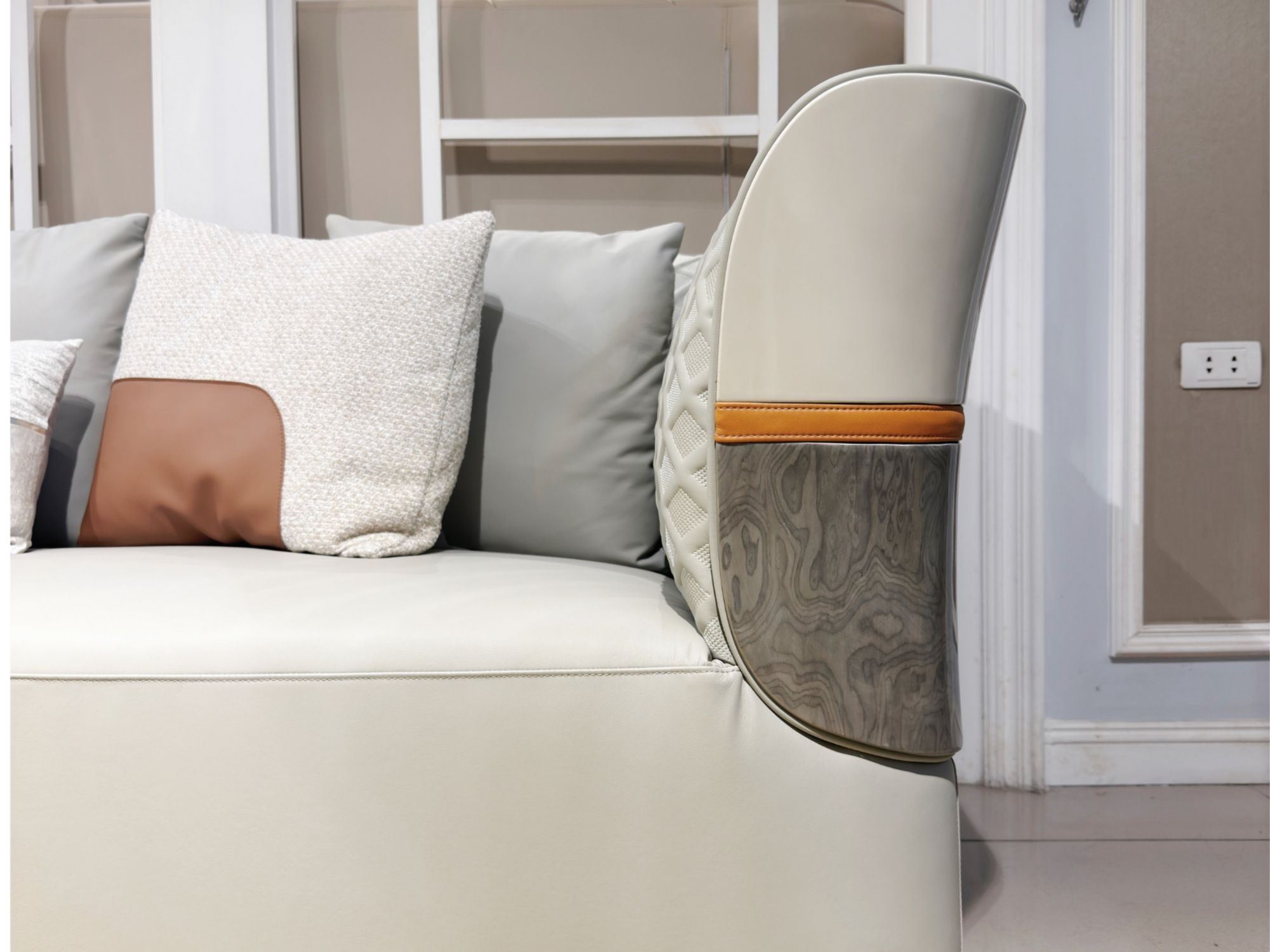 Chi tiết tay vịn sofa nhìn từ phía sau, cho thấy đường cong mềm mại của phần tựa lưng bọc da màu trắng kem. Phần ốp gỗ vân…