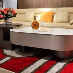 Bàn trà đôi LUNEA trong bối cảnh phòng khách sang trọng với sofa da màu kem, thảm đỏ họa tiết nổi bật. Trên bàn có bình ho…