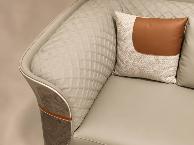 Cận cảnh góc ghế sofa IMPERIO SFGD52-123, tập trung vào phần tựa lưng chần trám và gối tựa nhỏ màu nâu cam. Phần ốp gỗ vân…
