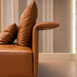 Cận cảnh tay vịn sofa màu nâu da bò, thiết kế bo tròn mềm mại và dày dặn, mang lại cảm giác êm ái. Gối tựa lưng cùng màu đ…