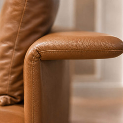 Chi tiết góc tay vịn của sofa màu nâu da bò, thể hiện chất liệu da căng mịn và đường may tinh xảo. Thiết kế góc cạnh được…
