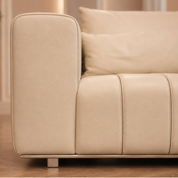 Góc chụp cận cảnh phần tựa lưng và tay vịn của sofa màu kem, với các đường may dọc tạo khối rõ ràng. Gối tựa lưng êm ái đư…