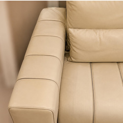 Cận cảnh góc sofa màu kem, với phần tựa lưng và tay vịn được thiết kế liền mạch, tạo khối vững chãi. Đường may nổi bật chạ…