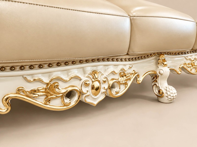Cận cảnh phần chân ghế và đường viền dưới của sofa VERSALÉON, với các họa tiết chạm khắc mạ vàng chạy dọc theo khung gỗ…