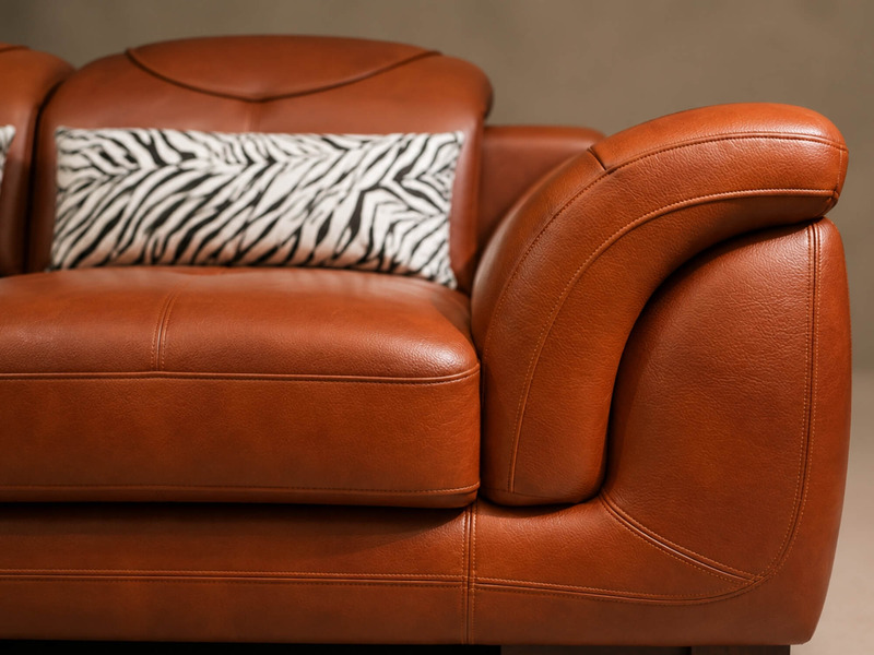 Cận cảnh phần tựa lưng và tay vịn của sofa góc màu nâu da bò, với gối tựa họa tiết ngựa vằn đặt gọn gàng. Thiết kế tổng th…