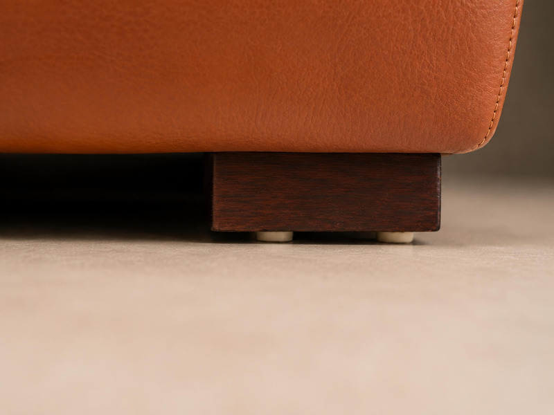 Cận cảnh chân sofa bằng gỗ màu nâu sẫm, thiết kế thấp và chắc chắn, nâng đỡ toàn bộ khung sofa. Chân gỗ được gia công tỉ m…