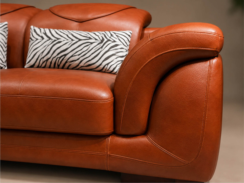 Cận cảnh tay vịn cong mềm mại của sofa góc màu nâu da bò, cho thấy chi tiết đường may tỉ mỉ và độ bóng tự nhiên của chất l…