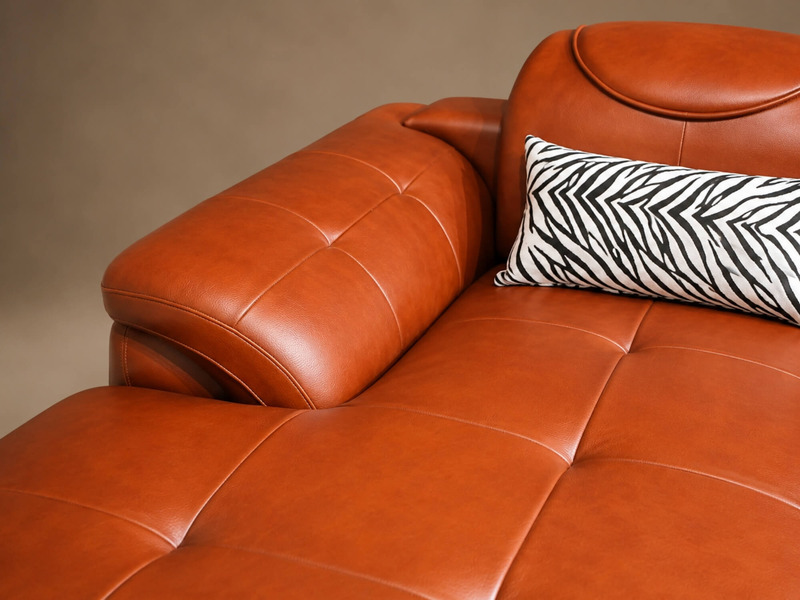 Cận cảnh phần đệm ngồi và tựa lưng của sofa góc màu nâu da bò, với các đường chần nút tinh tế trên bề mặt da. Chi tiết này…