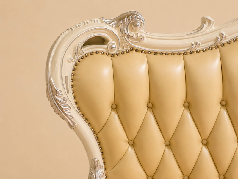 Cận cảnh góc trên bên trái của đầu giường MONARCHIA, cho thấy rõ phần khung gỗ màu trắng ngà với hoa văn chạm khắc tinh xả…