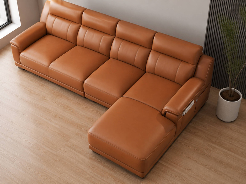 Sofa VENTO góc L màu nâu caramel, chụp từ góc thấp bên phải, làm nổi bật phần đệm ngồi và tựa lưng dày dặn. Các đường may…