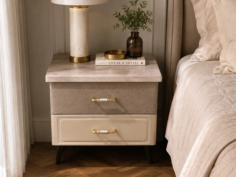Tab đầu giường HAZEL hiện đại, chụp chính diện trong phòng ngủ. Mặt tủ vân gỗ nhạt, ngăn kéo trên bọc vải màu nâu nhạt, ng…