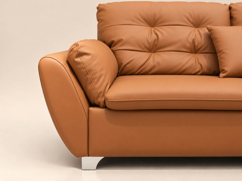Cận cảnh phần tay vịn và cạnh bên của ghế sofa ELVANE, cho thấy chất liệu da nhân tạo cao cấp màu nâu da bò với bề mặt mịn…